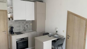 A compact kitchen with a built-in oven, a sink, and a small dining area with a chair and table. - Apartment Julia (Tisno)
