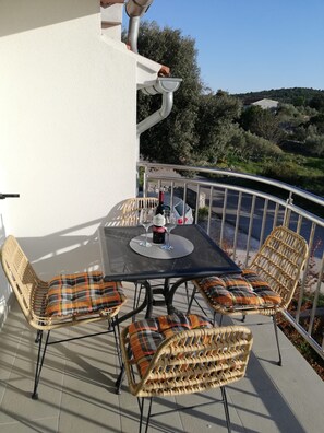 Une terrasse extérieure avec une table et des chaises en osier, une bouteille de vin et un verre.