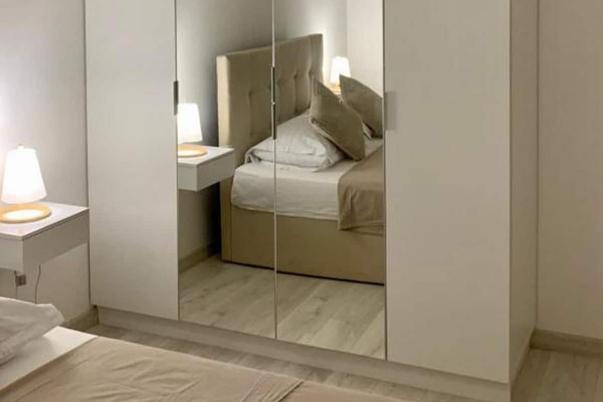 Une chambre avec une armoire à miroir, une table de chevet avec une lampe et un lit avec des oreillers.