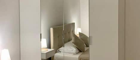 A bedroom with a mirrored wardrobe, a bedside table with a lamp, and a bed with pillows.