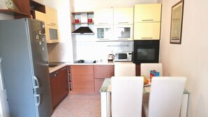 Een kleine keuken met een koelkast, magnetron, oven en een eethoek met twee stoelen en een tafel.