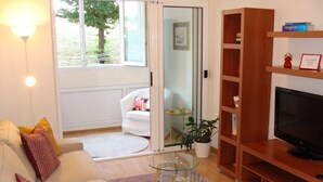 Een woonkamer met een witte bank, een glazen salontafel, een houten tv-meubel en een schuifpui naar een balkon.