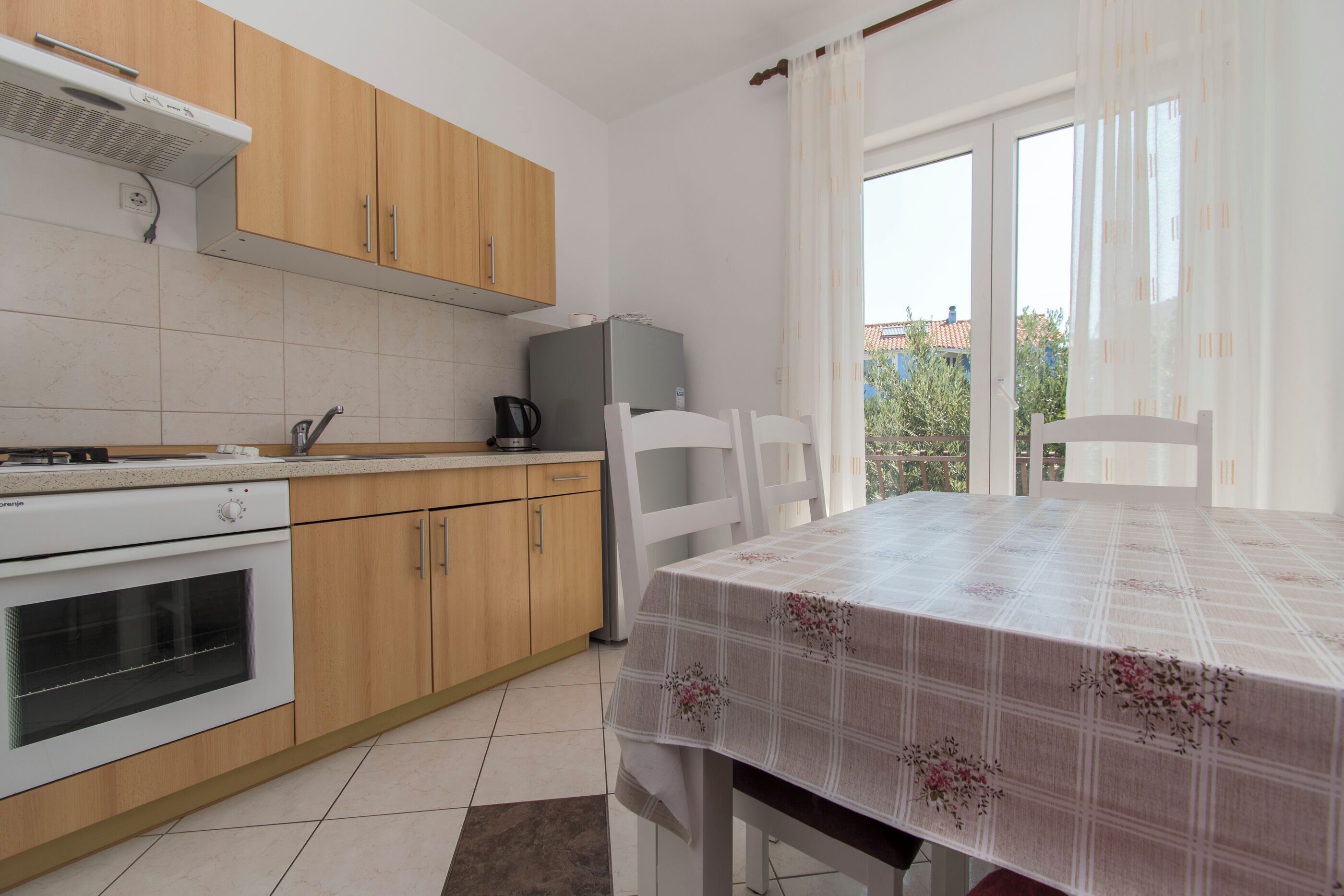 A kitchen with wooden cabinets, a built-in oven, a refrigerator, and a dining table with a floral tablecloth.