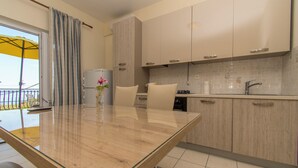 A modern kitchen with a glass-top dining table, beige cabinets, and a view of the outdoors. - Apartment Mila (Primosten)