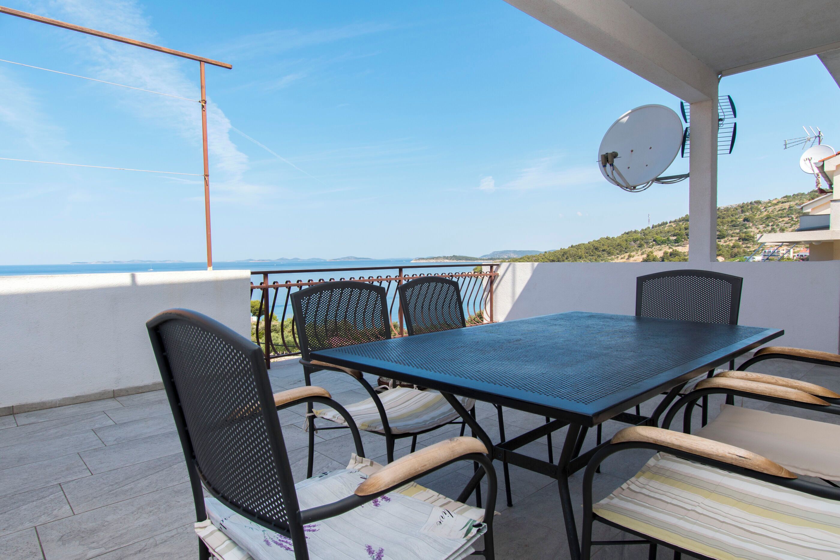 A terrace with a table and chairs, a satellite dish, and a view of the sea.