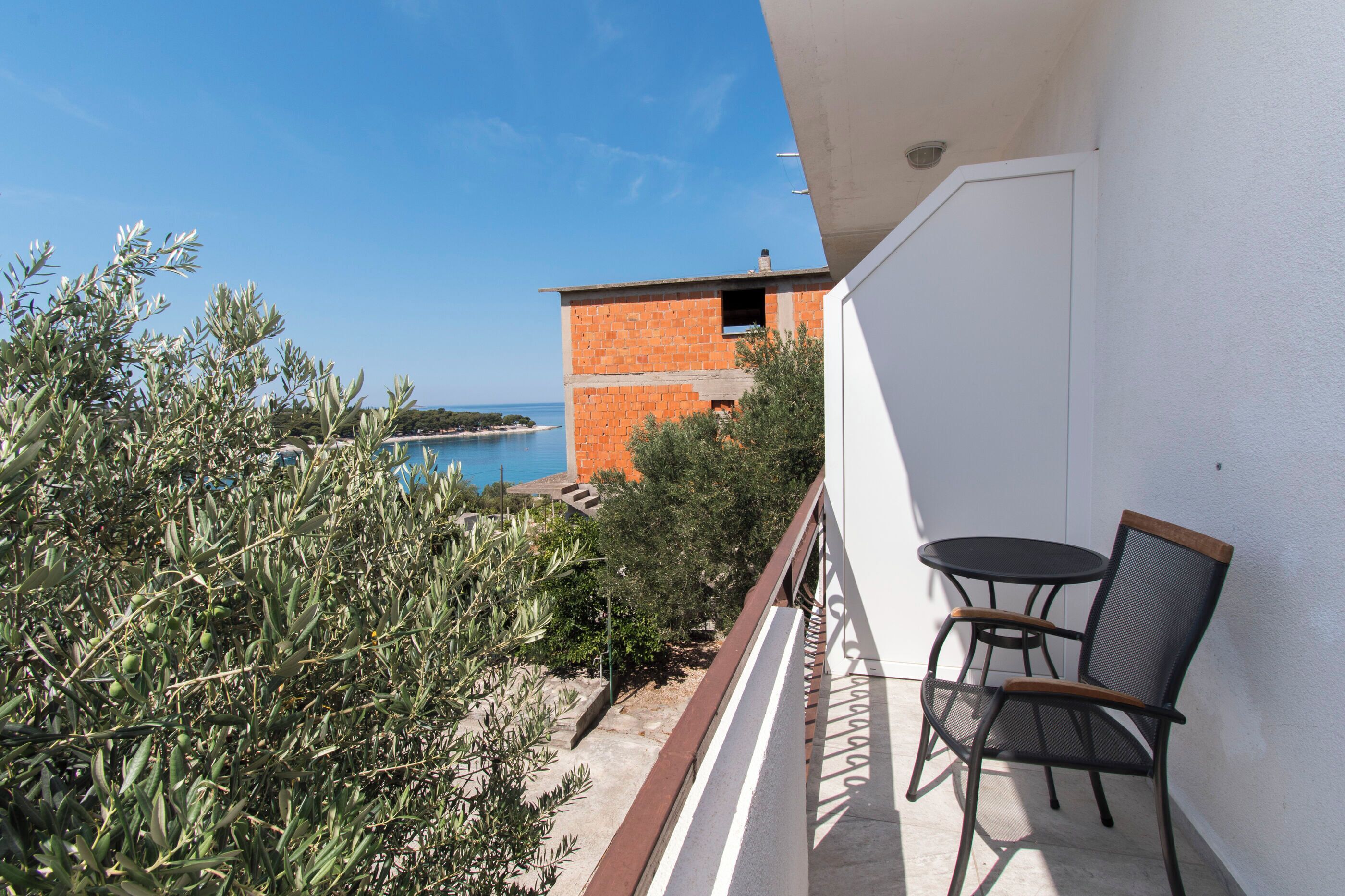 Un balcon avec une table et des chaises, d’où l’on peut admirer un ciel bleu dégagé et une vue lointaine sur un bâtiment et la côte.