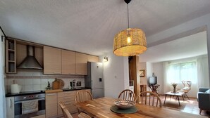 Et moderne køkken med træskabe, et rustfrit stål køleskab og et spiseområde med et træbord og stole.