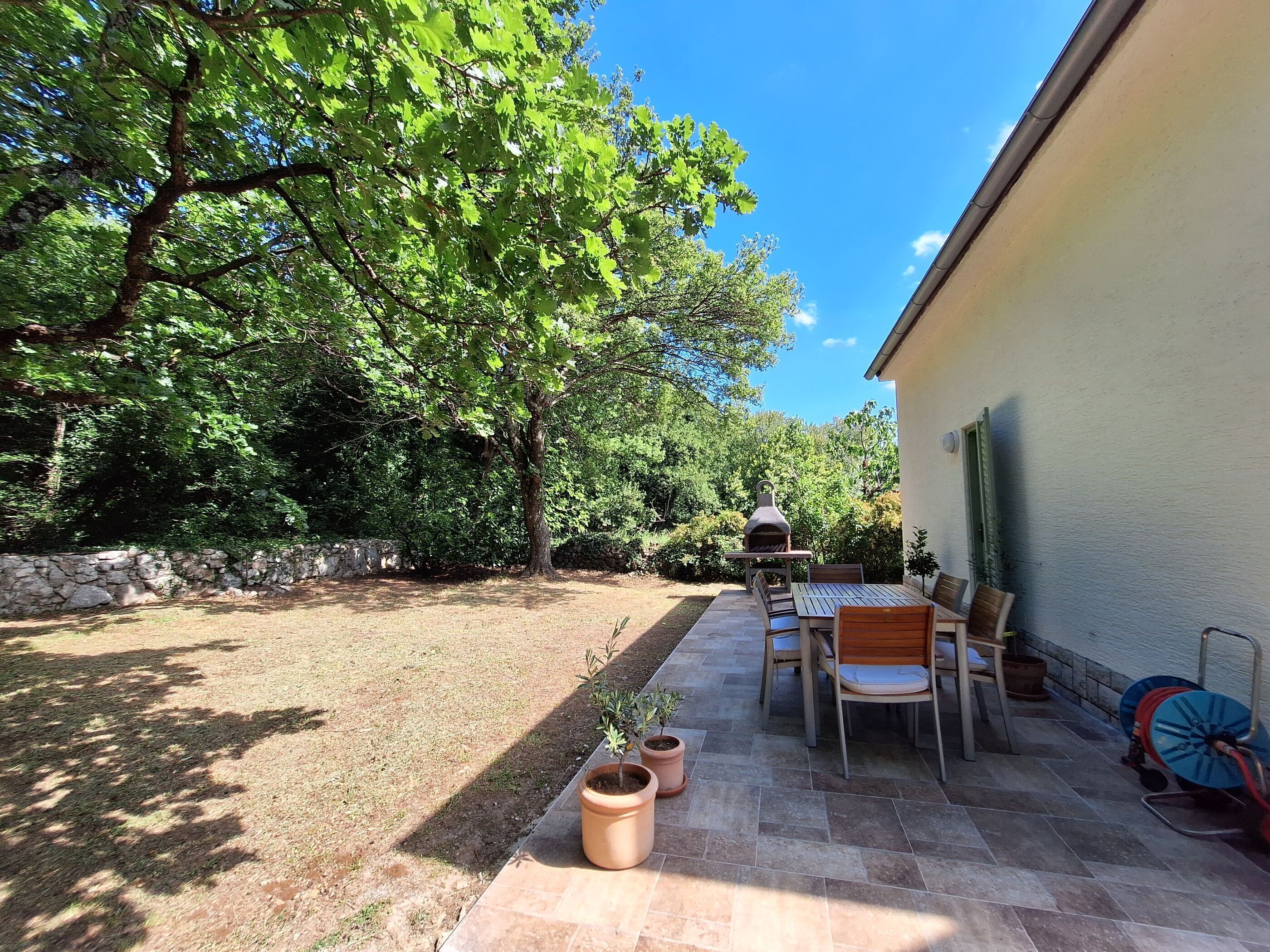 An outdoor patio with a barbecue grill, seating area, and potted plants.