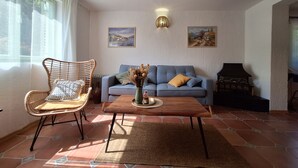En stue med en blå sofa, en fletstol og et sofabord. To billeder hænger på væggen, og der er en pejs.