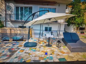 Eine Terrasse mit Mosaikboden, Sitzgelegenheiten im Freien und einem großen Sonnenschirm.