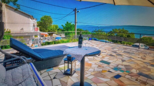 Eine Außenpatio mit Mosaikboden, einer Sitzecke mit Kissen, einer Laterne und Blick auf das Meer und Gebäude im Hintergrund.
