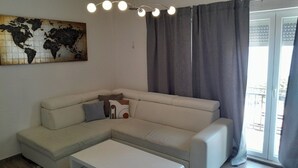 Ein modernes Wohnzimmer mit einer Eckcouch, einem Couchtisch, einer Weltkarte als Kunstwerk und einem großen Fenster mit Vorhängen.