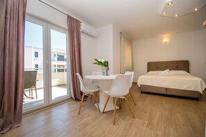 A hotel room with a bed, a dining table with chairs, a potted plant, and a view through the glass door. - Apartment Marija (Vodice)