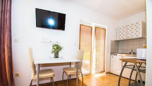 Cucina compatta con angolo ristoro, TV a parete e porta scorrevole che dà su un balcone.