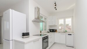 A modern kitchen with white cabinetry, a built-in oven, a microwave, and a refrigerator. - Apartments Quokka (Tribunj)