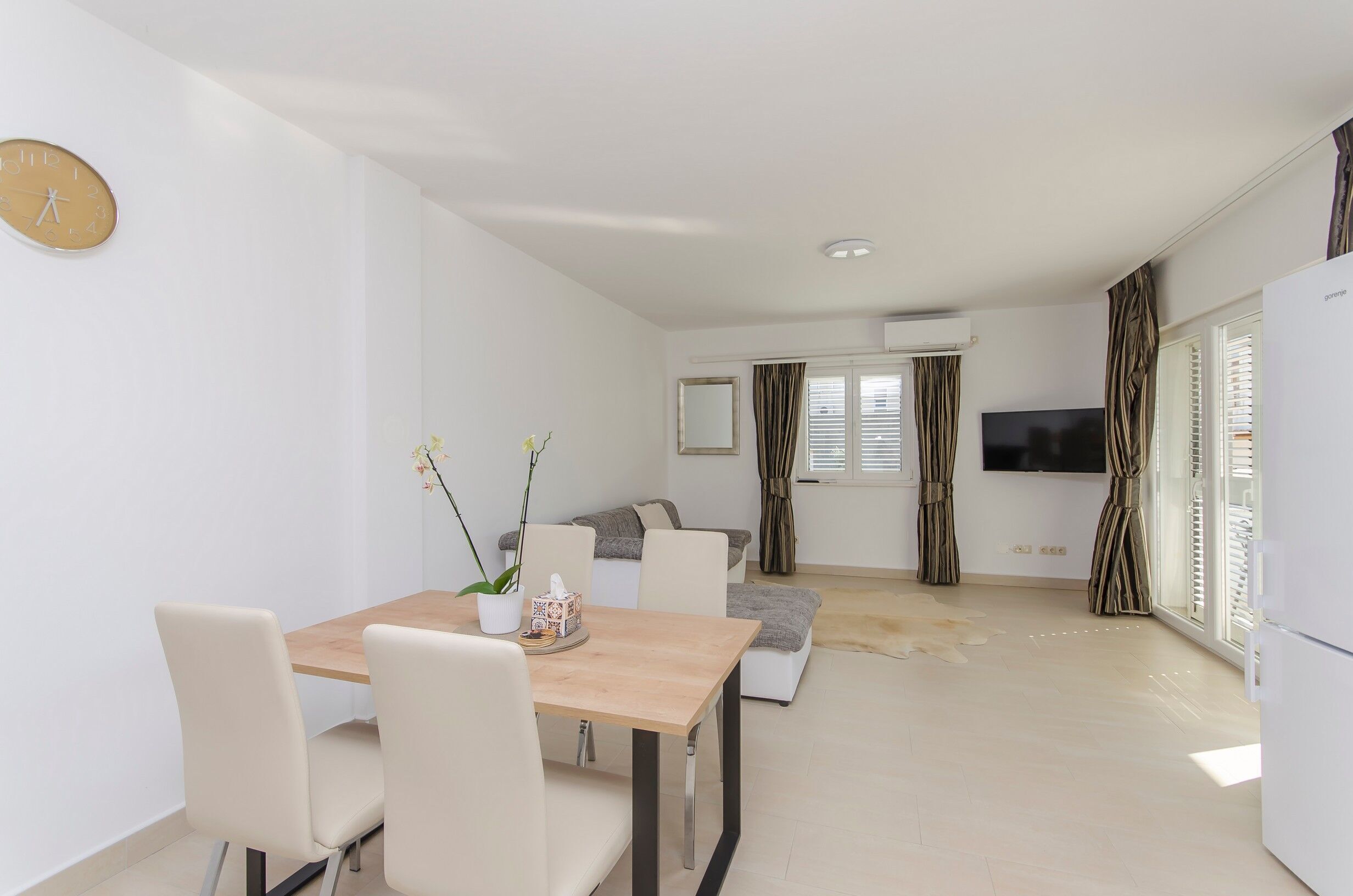 A modern living room with a sofa, a dining table with chairs, a TV, and a refrigerator.