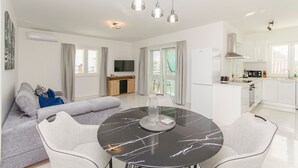 A modern apartment with a dining area featuring a marble table, a grey sofa with cushions, and a kitchen with white cabinets and a built-in oven. - Apartments Quokka (Tribunj)