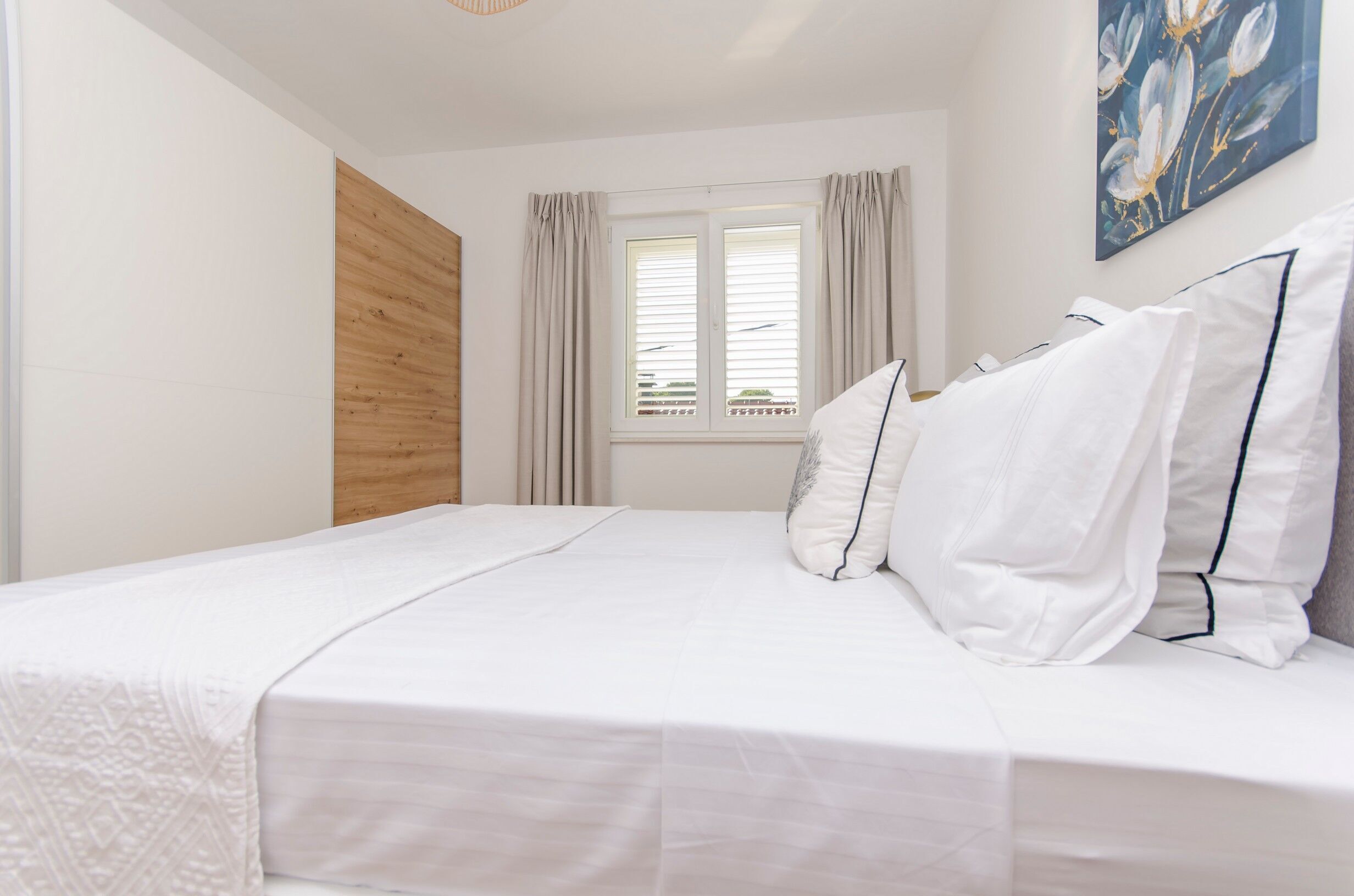 A bedroom with a bed, a wooden panel wall, a window with curtains, and a painting on the wall.