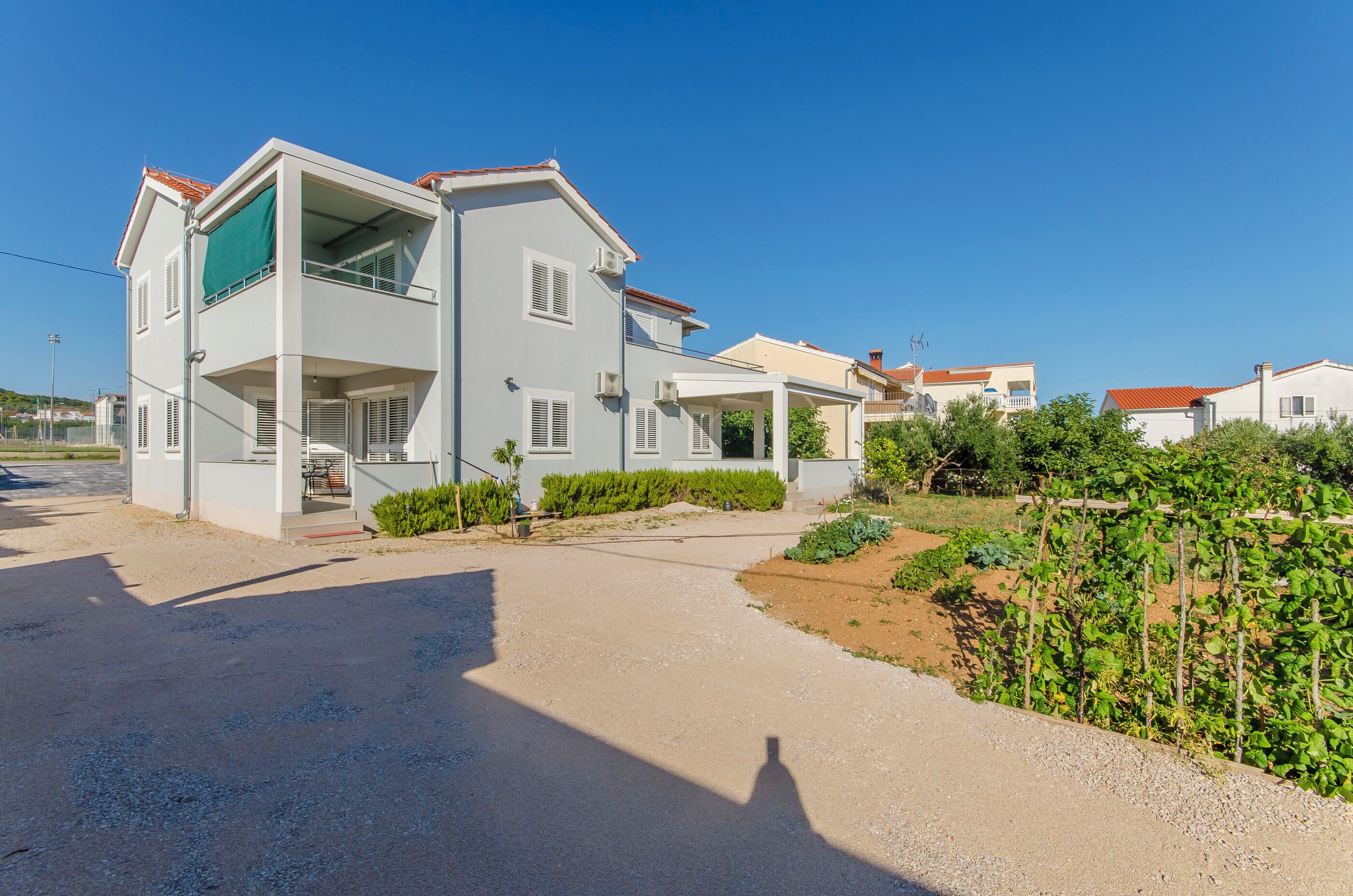 Ein zweistöckiges Wohnhaus mit überdachter Terrasse, einem Schotterweg und einem Garten mit Pflanzen.