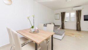 A modern living room with a dining table, white chairs, a sofa, and a large window with curtains. - Apartments Quokka (Tribunj)