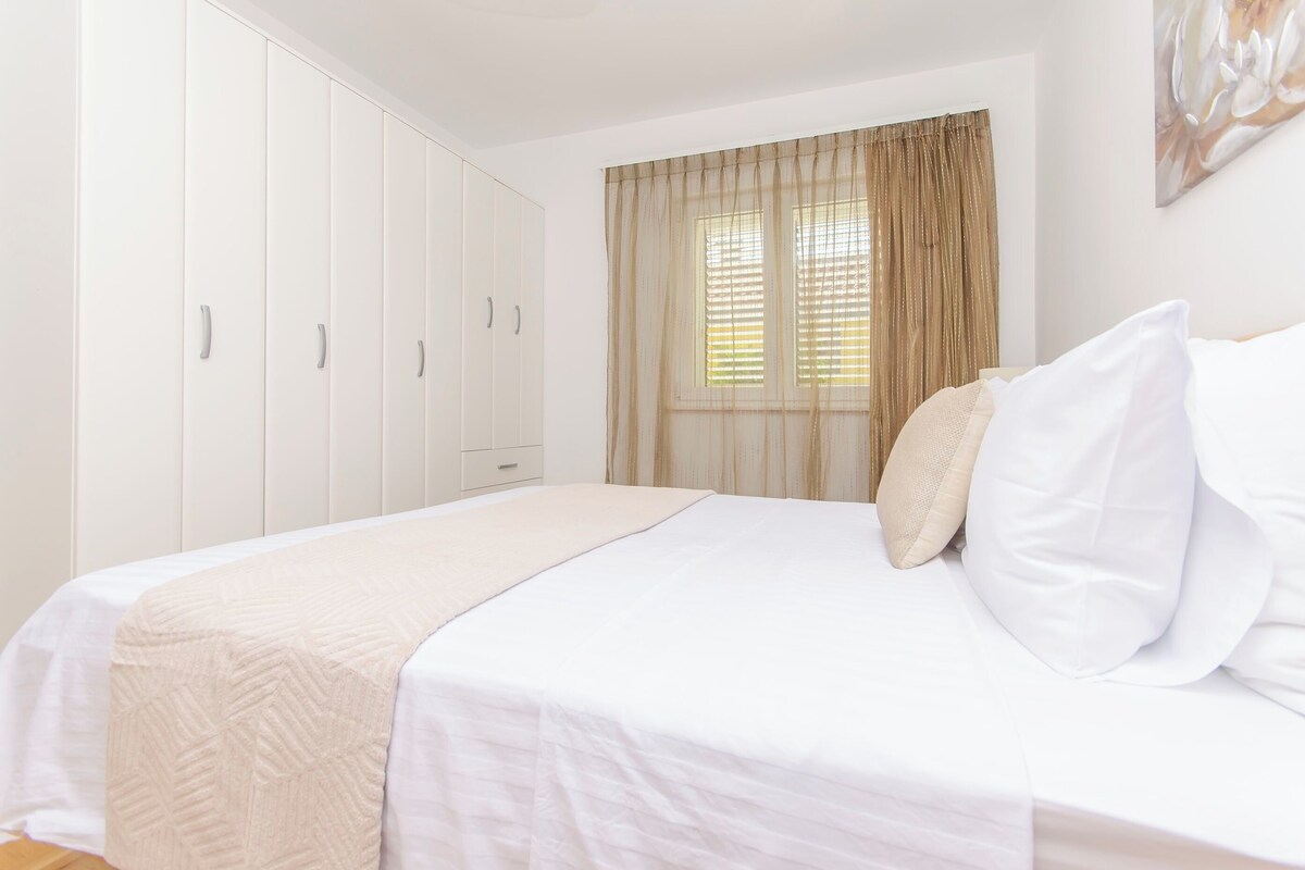 A bedroom with a bed, white wardrobe, and a window with curtains.