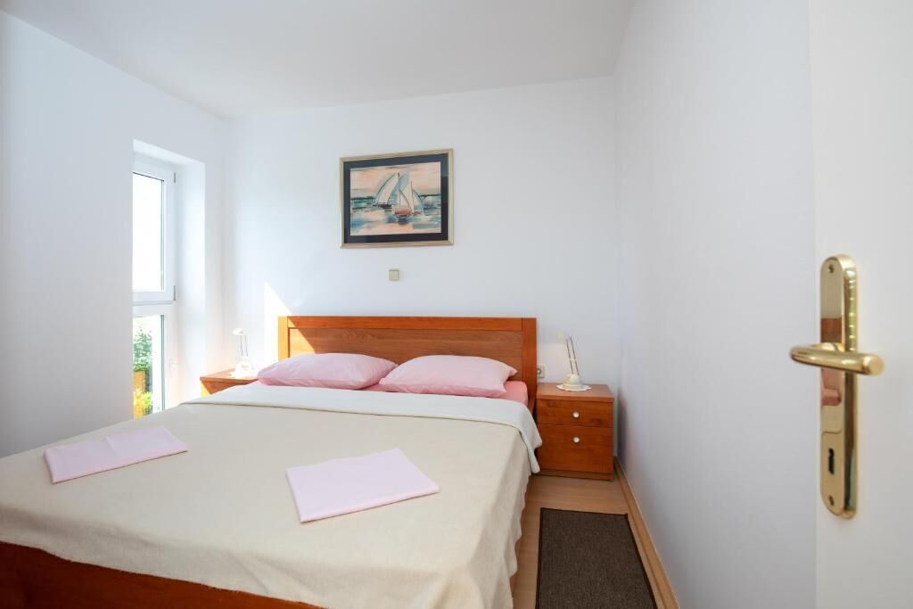 A bedroom with a bed, a nightstand, a lamp, a framed picture on the wall, and a door with a golden handle.