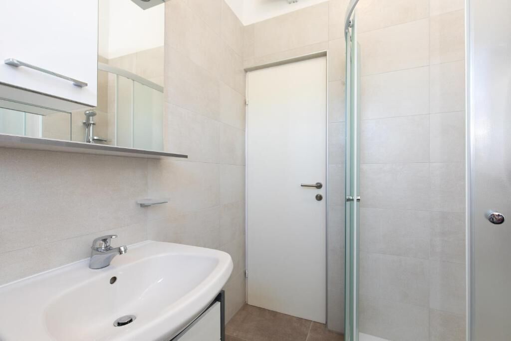 Un baño con un lavabo blanco, un espejo y una cabina de ducha con paredes de cristal.