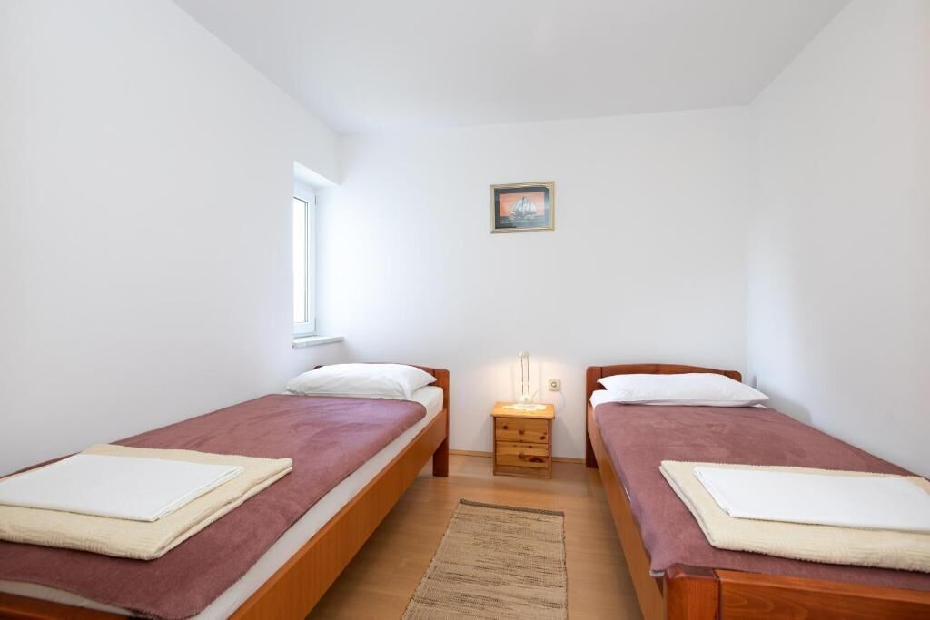A small, clean room with two single beds, a nightstand, and a window.