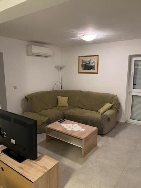 Un salon avec un canapé d’angle beige, une table basse en bois, un téléviseur à écran plat posé sur un meuble en bois, une lampe sur pied et un tableau encadré accroché au mur.