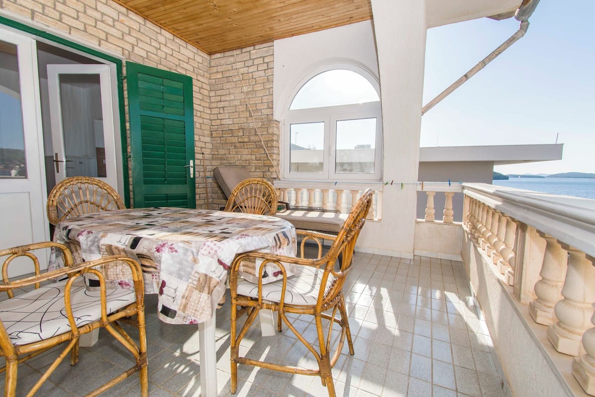 A balcony with wicker furniture, a table with a floral tablecloth, and a view of the sea.