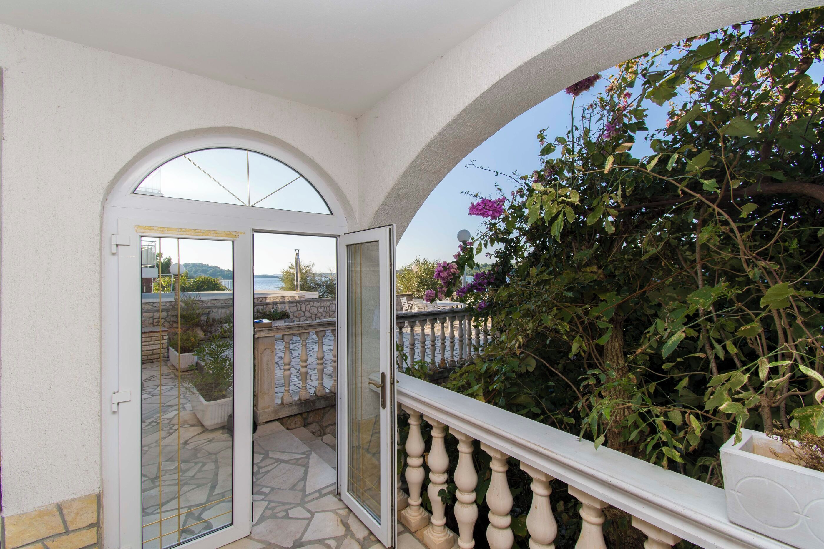 A balcony with a stone floor, white balustrade, and a view of greenery and a distant landscape.