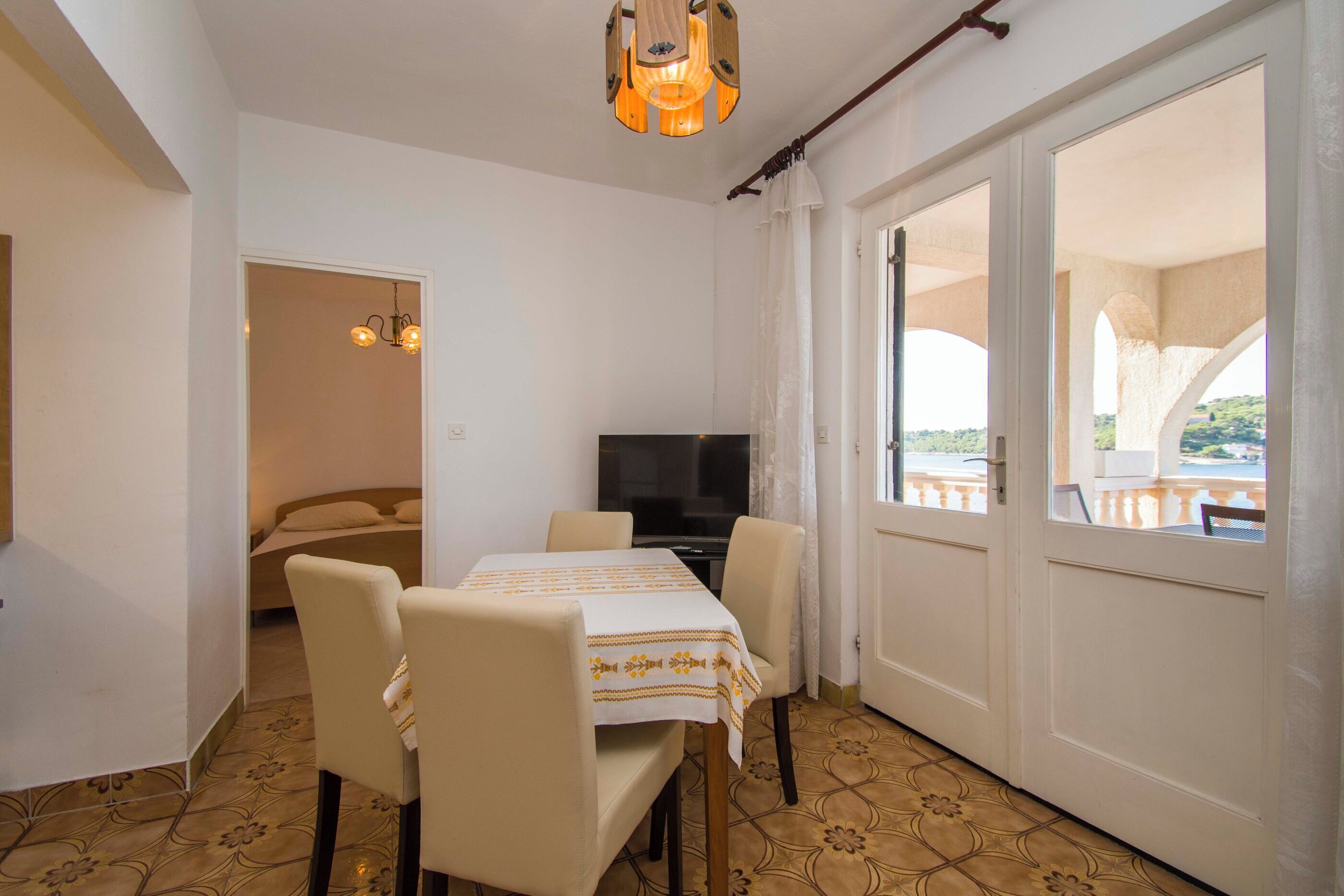 Quarto com mesa de jantar, cadeiras, televisão e varanda com vista.