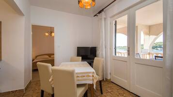Quarto com mesa de jantar, cadeiras, televisão e varanda com vista.