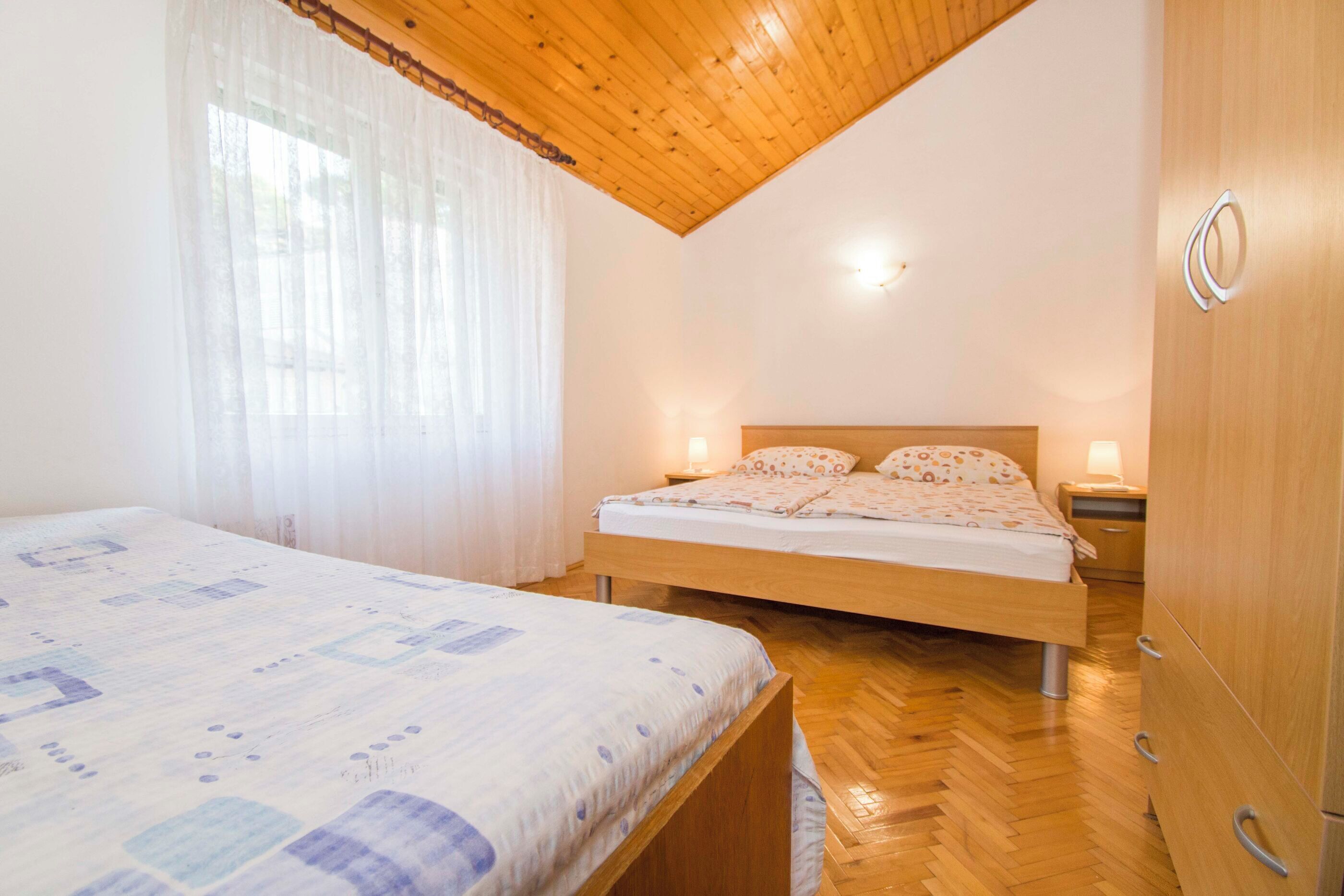 Um quarto com teto de madeira, cama com colcha estampada, mesa de cabeceira e guarda-roupa.