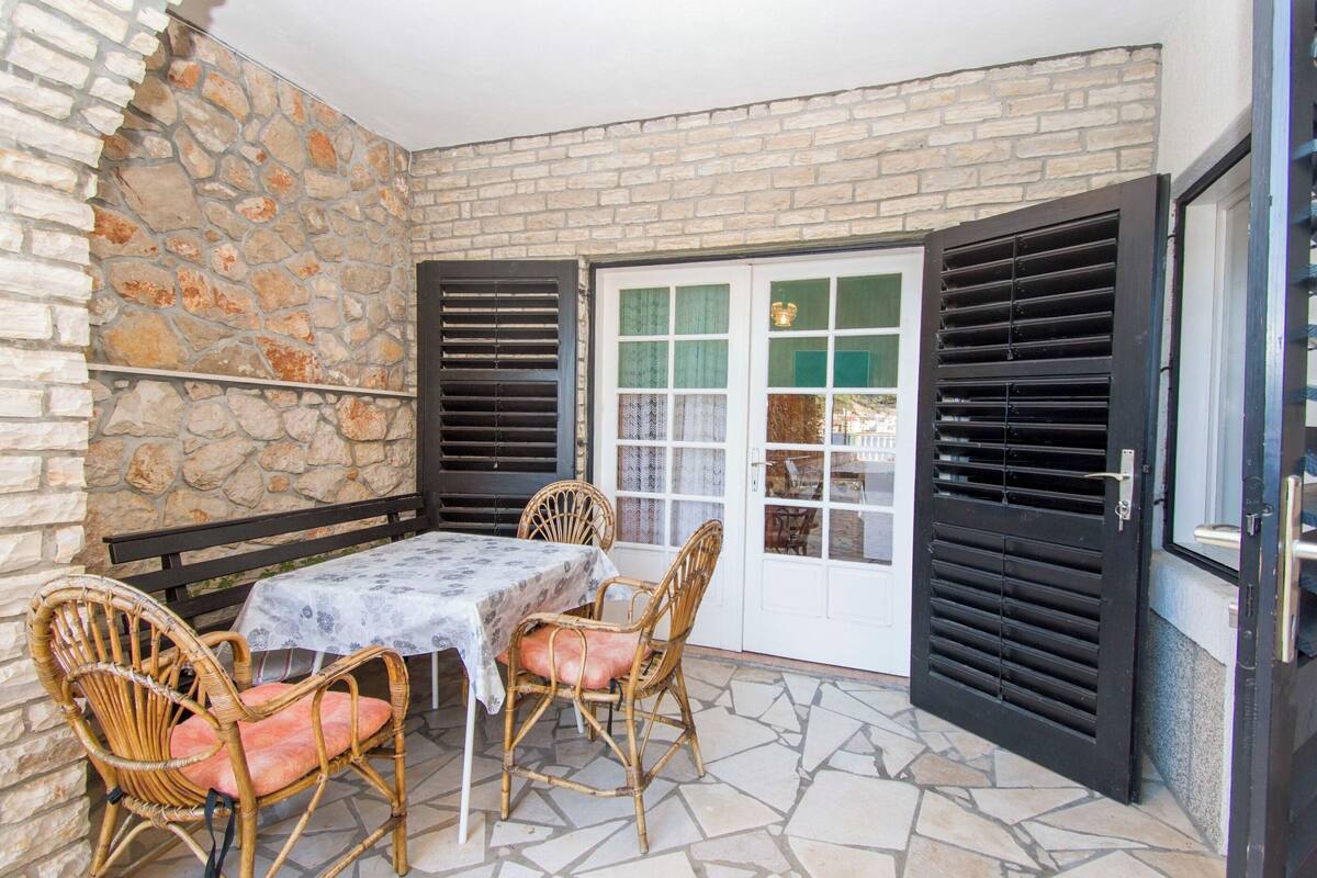 A patio with a stone wall, a table with chairs, and a door with shutters.