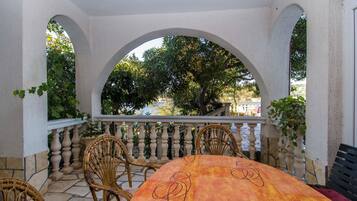Un área de comedor al aire libre con techo, que incluye una mesa y sillas, rodeada de arcos y una barandilla.