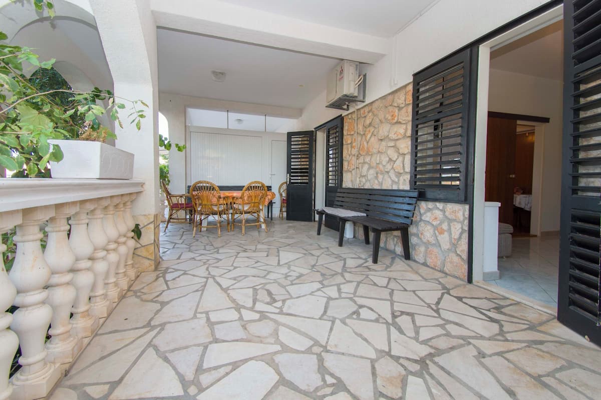 A stone-tiled patio with a dining table and chairs, a bench, and a potted plant.