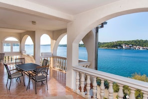 Portico coperto con tavolo e sedie, affacciato su uno specchio d'acqua e una costa lontana.