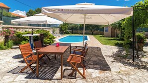 Een buitenzwembad met een tafel en stoelen, omringd door parasols en groen.
