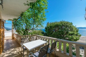 Un balcon avec une table et des chaises, donnant sur une zone côtière bordée d’arbres et offrant une vue sur un ciel dégagé.