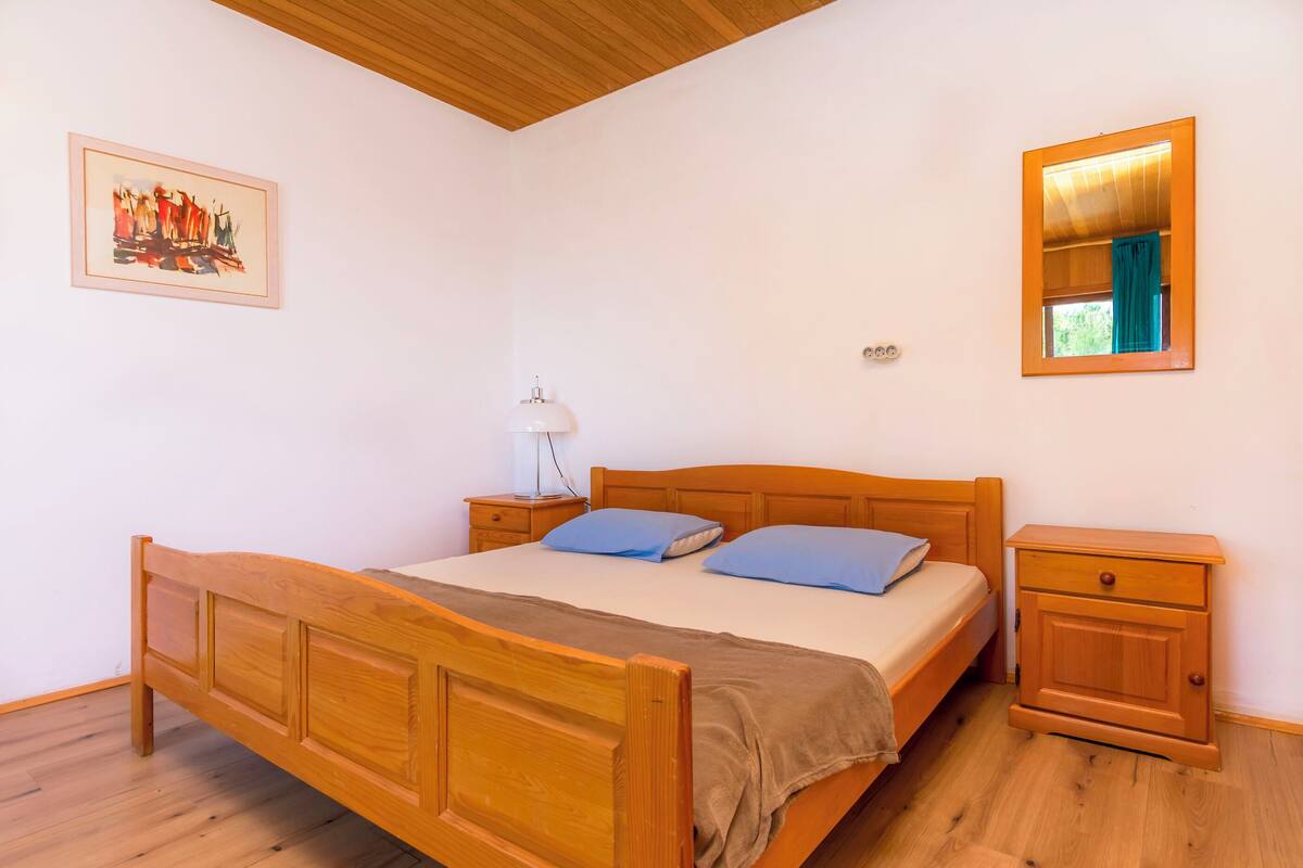 Un dormitorio con una cama de madera, una mesita de noche, un tocador, un espejo y un cuadro en la pared.