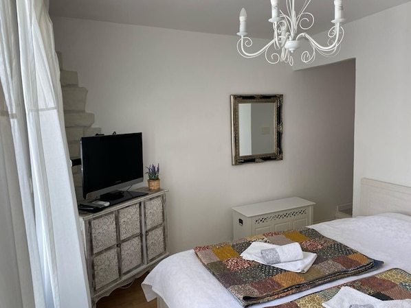 A bedroom with a bed, a television on a cabinet, a mirror, and a chandelier. - House Shabby (Crikvenica)
