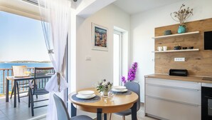 A modern kitchen with a wooden countertop, a dining area with a round table and chairs, and a view of the sea through large windows. - Apartments Doro (Blato)