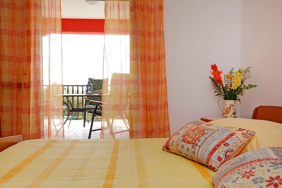 A bedroom with a bed, a nightstand, a vase with flowers, and a view of an outdoor balcony.