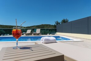 Un verre rempli de boisson sur une table près d’une piscine, avec des chaises longues et une serviette.
