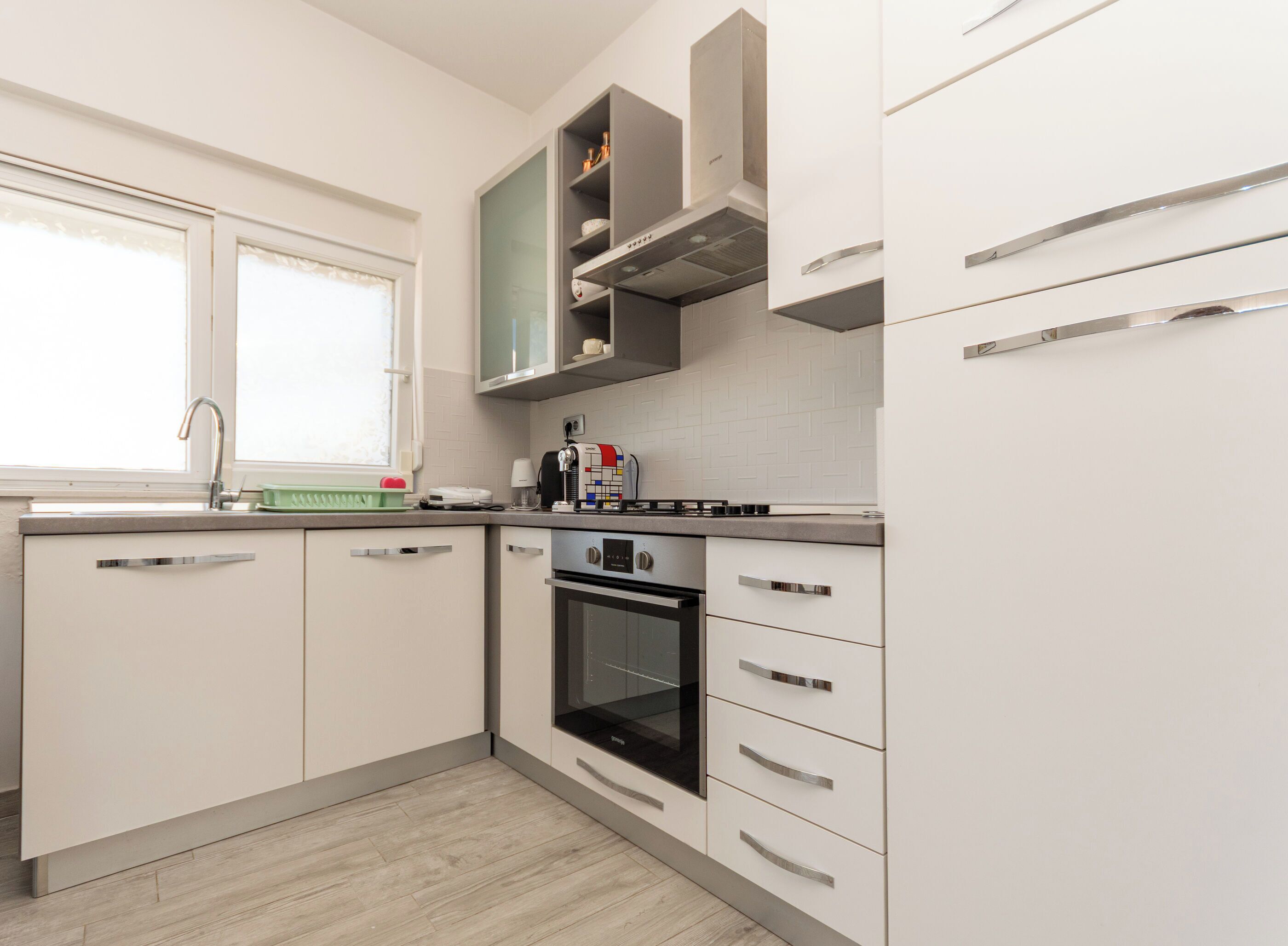 Une cuisine moderne avec des meubles blancs, un four encastré et une fenêtre offrant une belle vue.