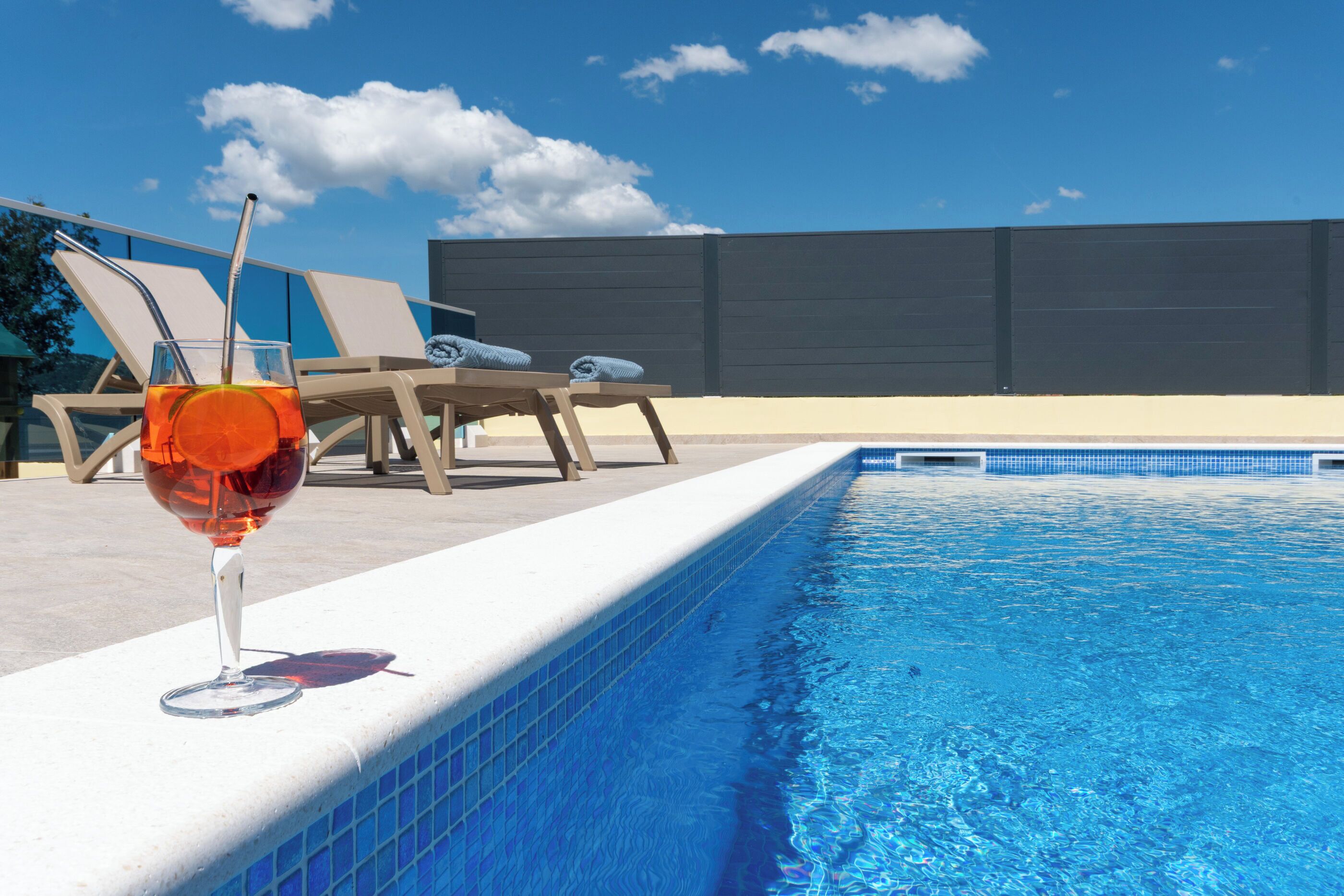 A swimming pool with lounge chairs and a glass of red drink.