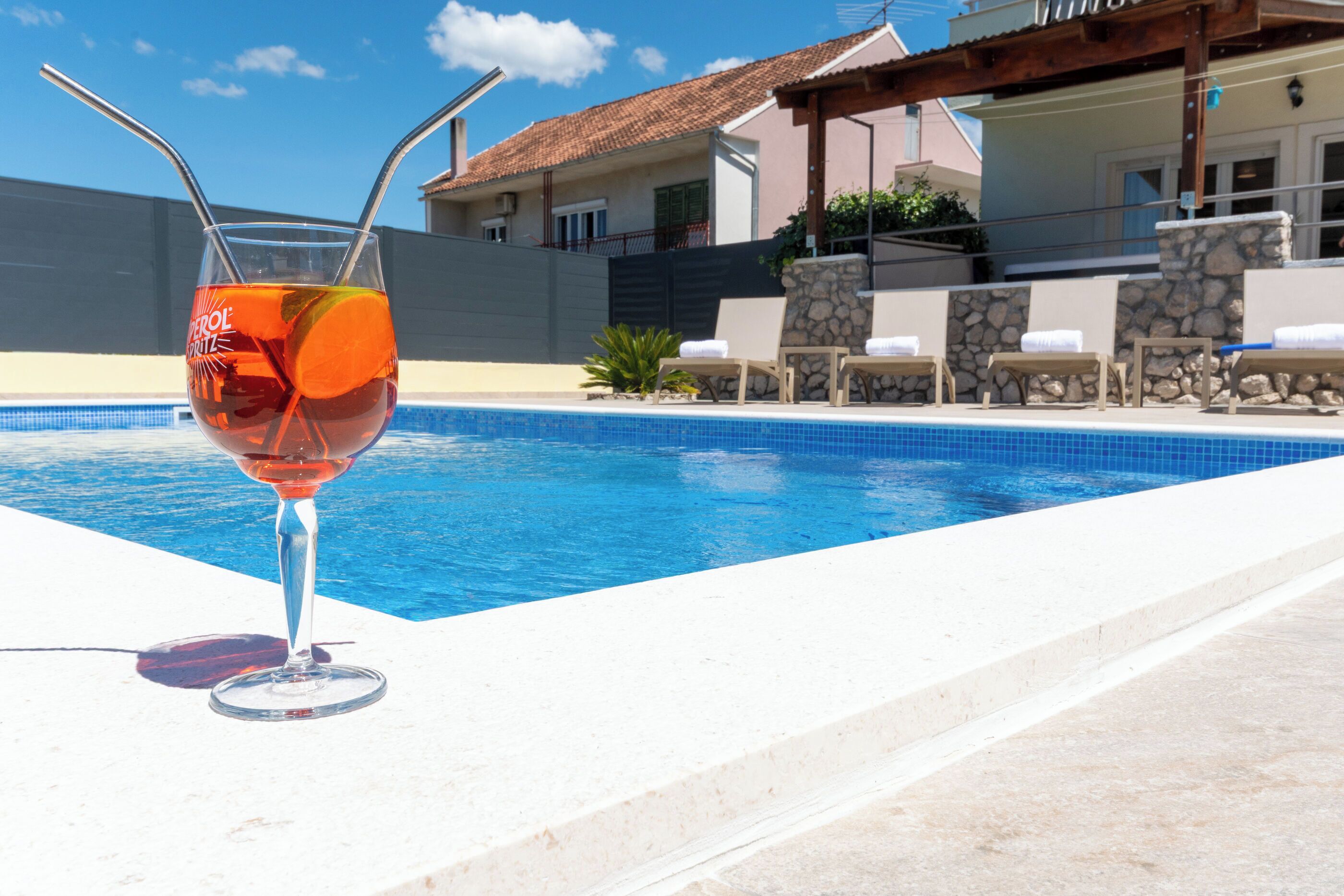 A swimming pool with lounge chairs and a glass of drink.