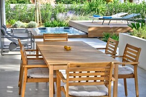 Ein Holzes-Esstisch mit gepolsterten Stühlen, ein Whirlpool und Liegestühle in einem Garten.