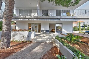 Ein modernes, zweistöckiges Haus mit einem Balkon, einer Terrasse mit Gartenmöbeln und einem angelegten Garten.